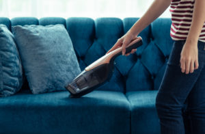 Close up of A woman housewife vacuuming furniture in a house with a hand-held portable vacuum cleaner